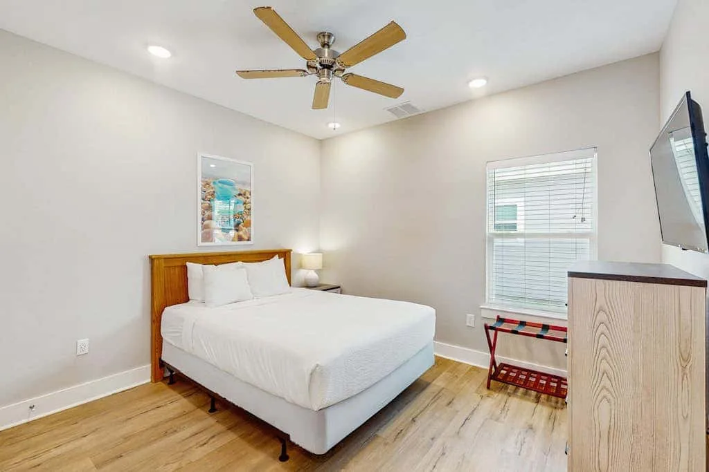 Un dormitorio luminoso con una cama, un ventilador de techo y una ventana.