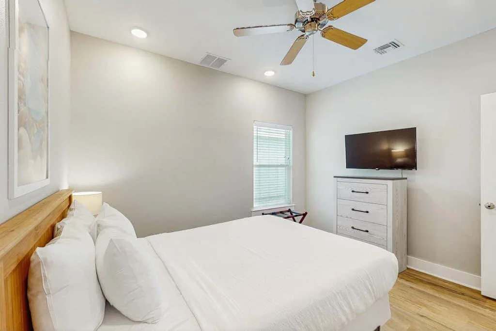 Un dormitorio luminoso con una cama bien hecha y un televisor sobre una cómoda.