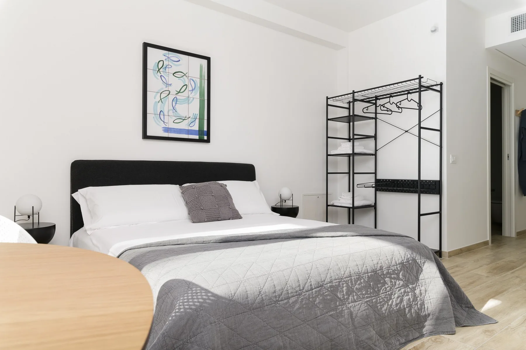 A bright bedroom with a neatly made bed and black open clothes rack.