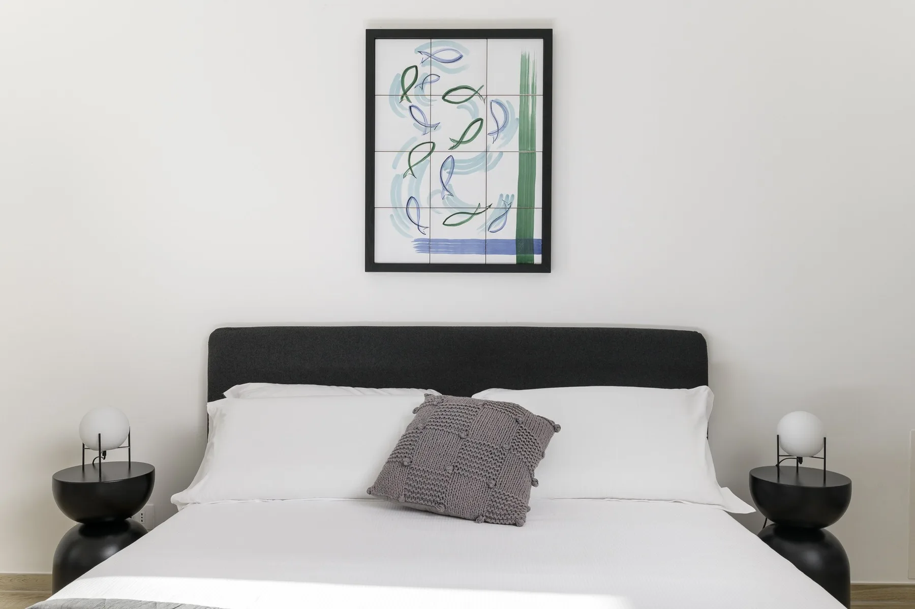 A bedroom with a bed, white bedding, and framed artwork above the headboard.