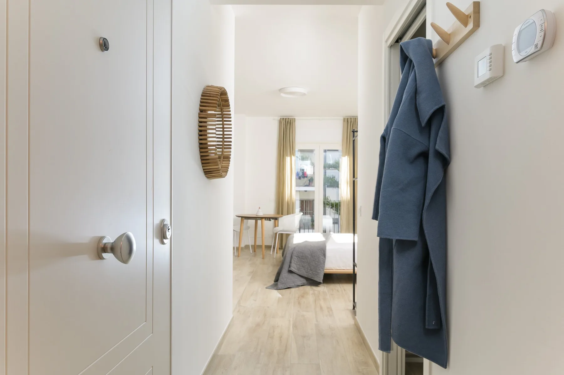 Se ve un dormitorio más allá de la puerta, con una cama y una pequeña mesa de comedor.