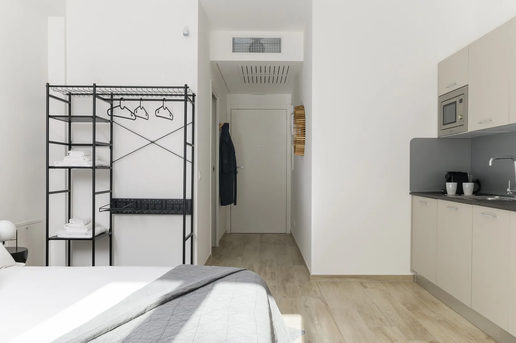 Un dormitorio con una cama, un perchero abierto y una pequeña cocina junto a la pared.