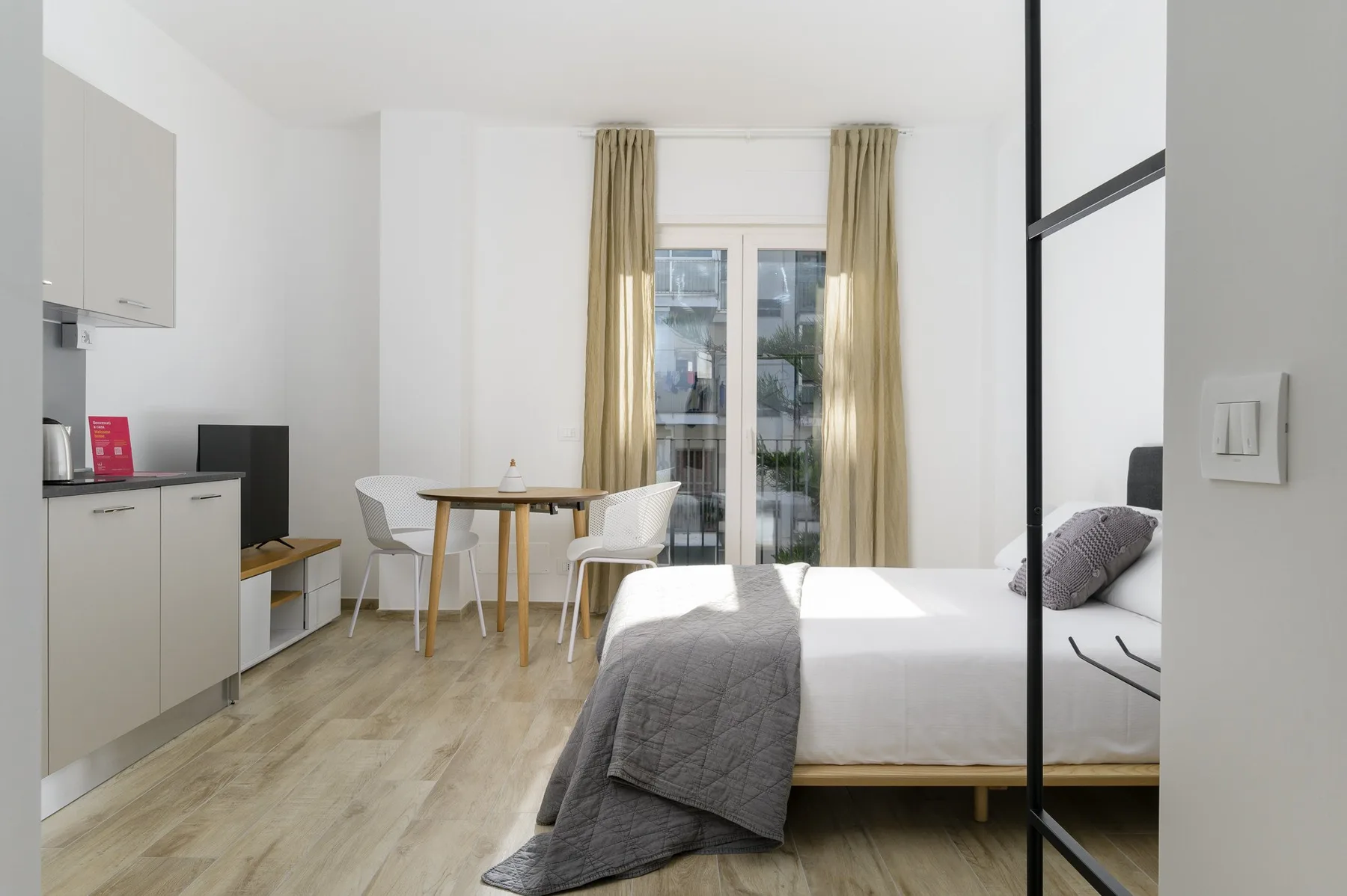 Un dormitorio luminoso con una cama, una mesa pequeña y cortinas junto a la ventana.