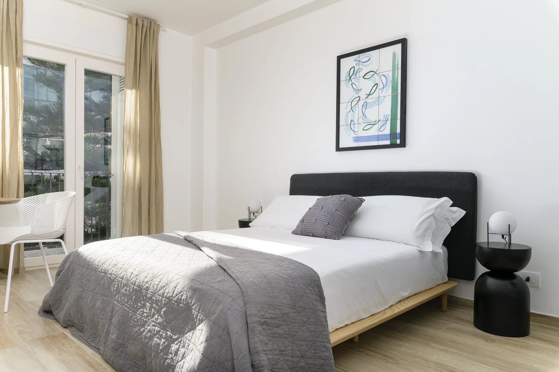 Un dormitorio luminoso con una cama bien arreglada y un cuadro sobre el cabecero.