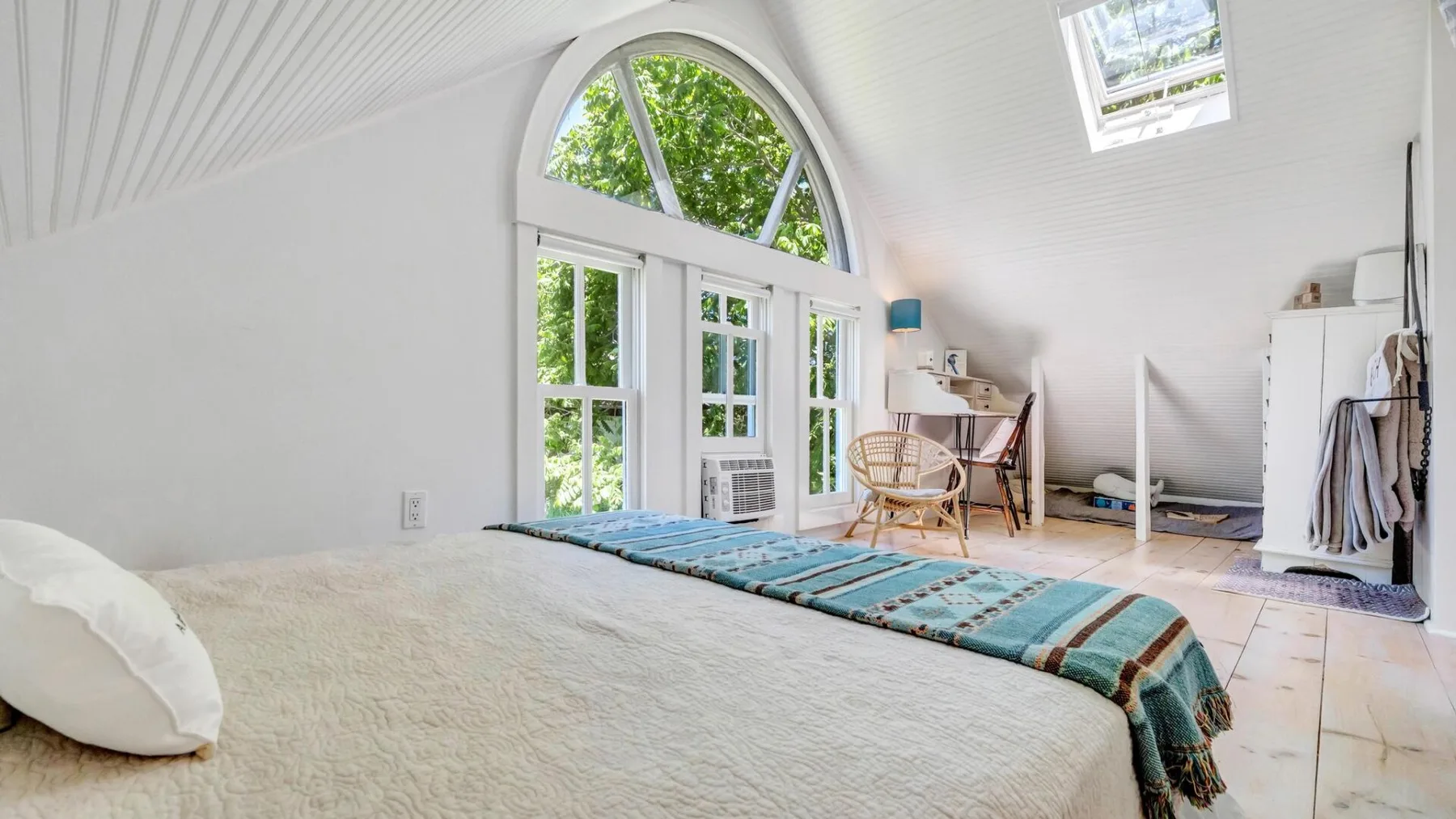 A bright bedroom with a bed beside large arched windows.