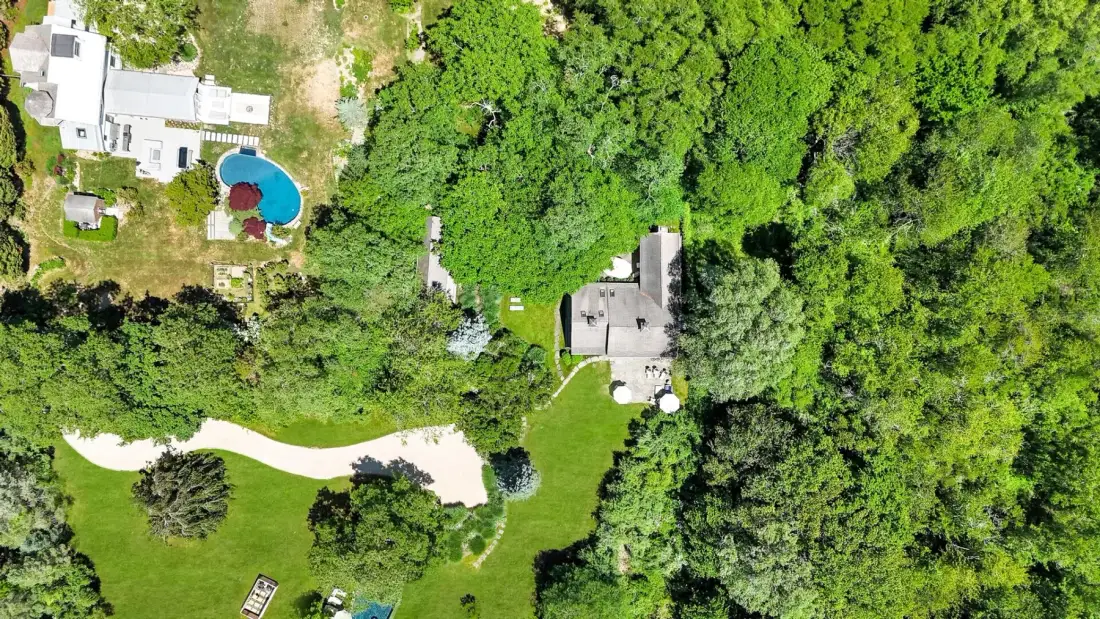 An aerial view shows a house surrounded by dense trees and a winding driveway.