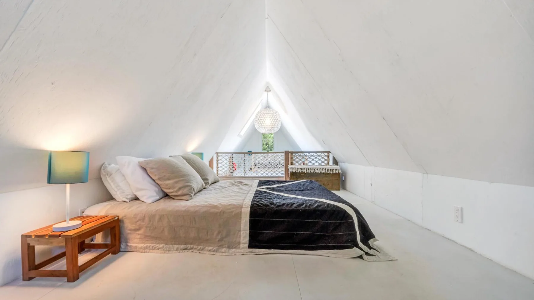 A bed sits beneath the sloped ceiling of a bright attic bedroom.