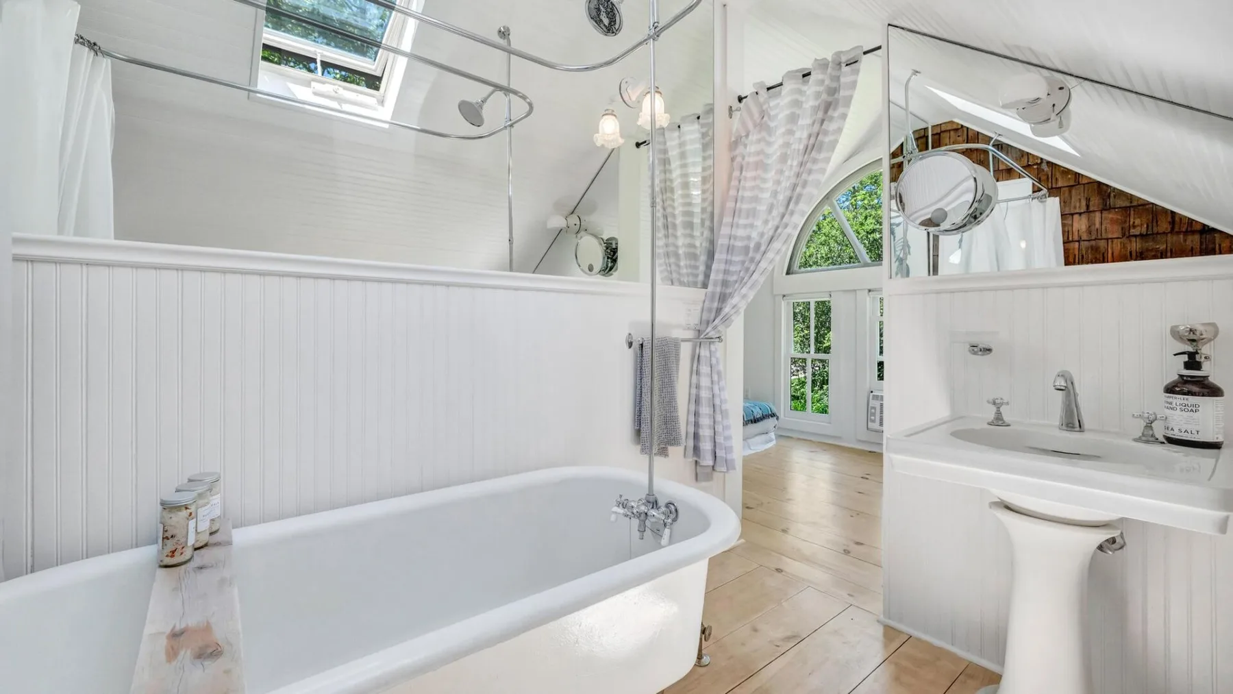 A bright bathroom with a bathtub, sink, and arched window.