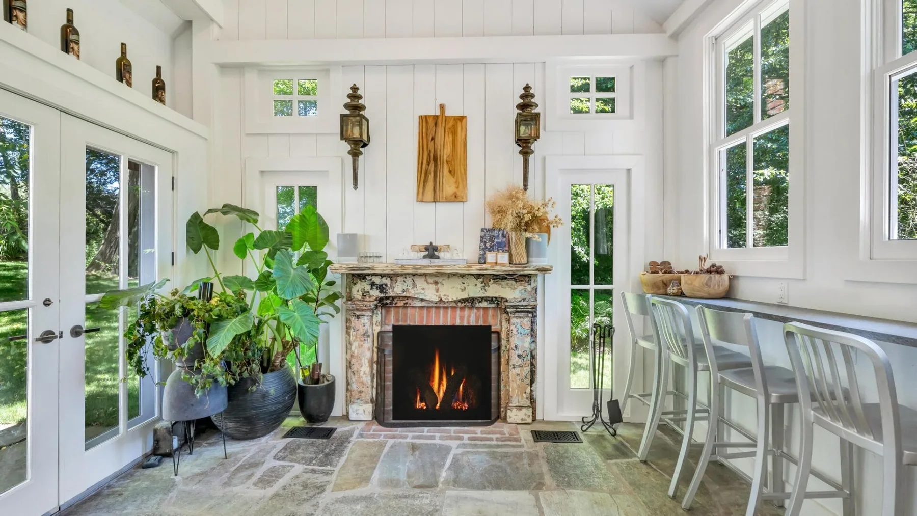 A bright sunroom features a stone fireplace, glass doors, and seating at a counter.