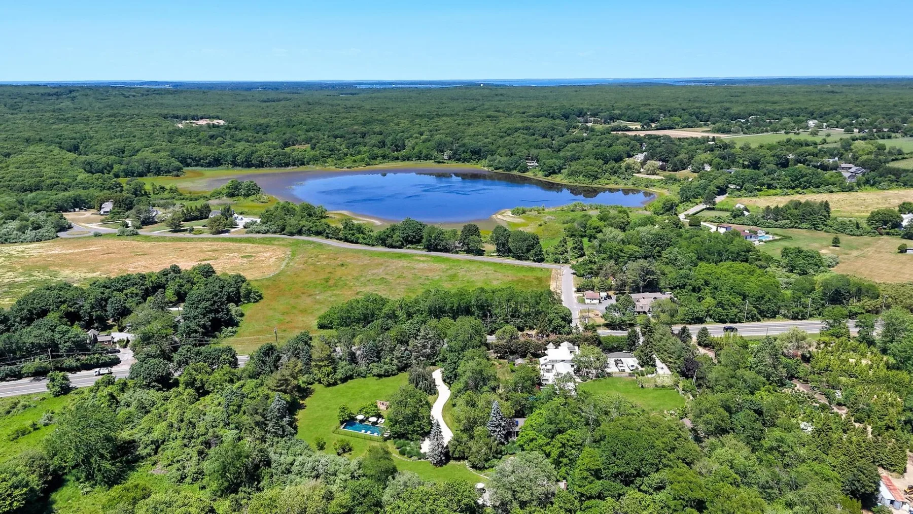 Aerial view of a wooded landscape with a lake and scattered buildings.