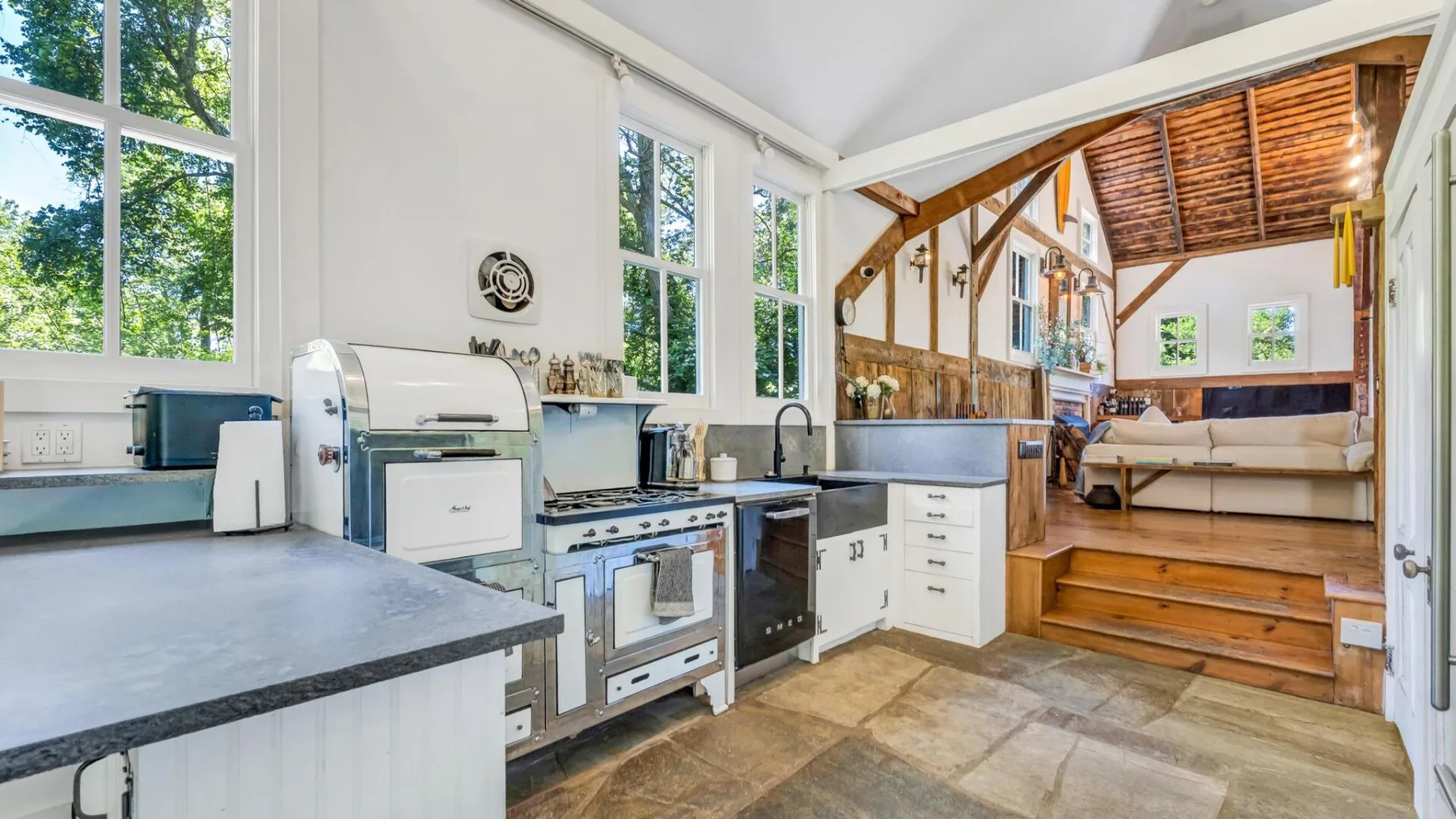 A bright kitchen with a stove and sink opens onto a raised seating area.