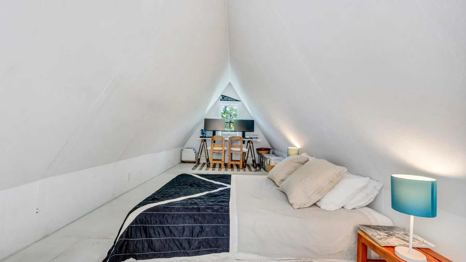 A small attic sleeping area with a bed and a table beneath the sloped ceiling.