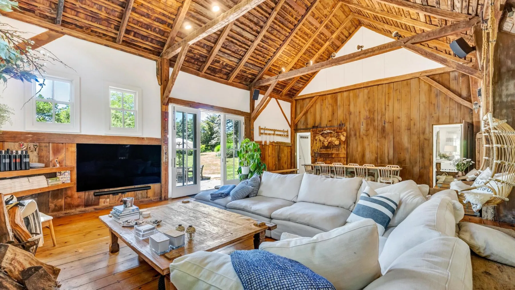 A bright living room with pale seating beneath an exposed timber roof.