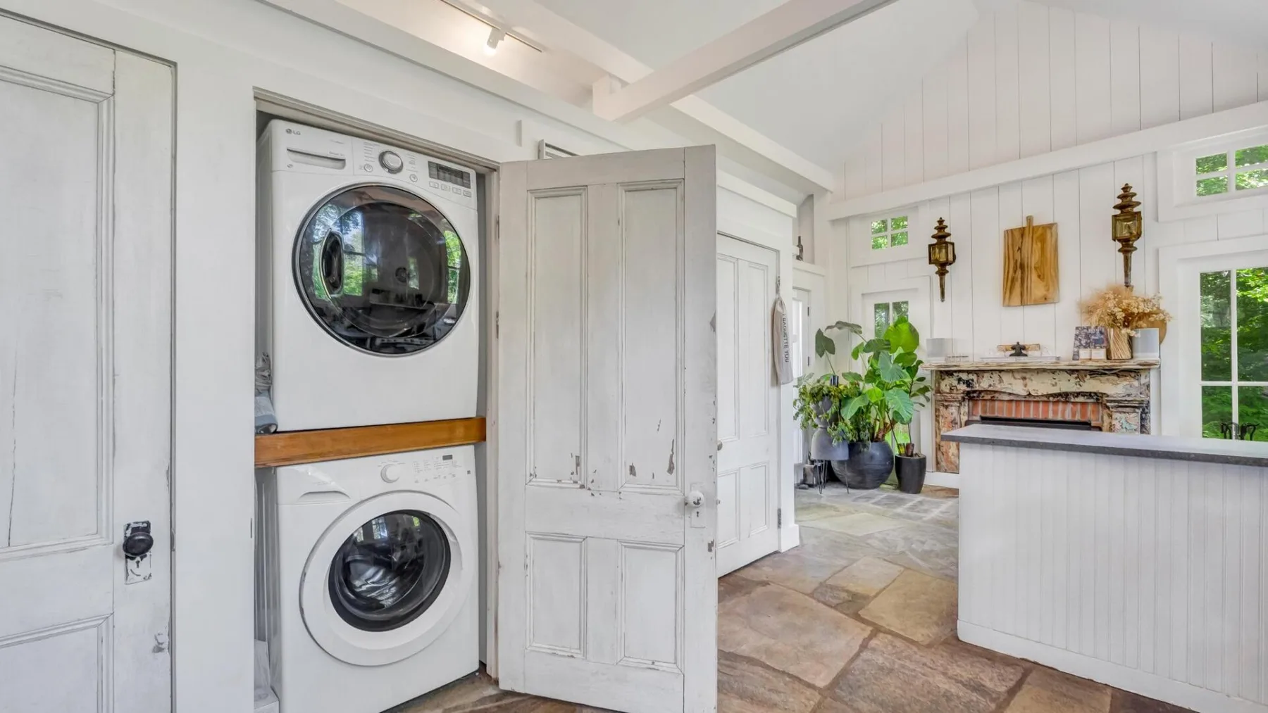 A bright laundry room with a stacked washer and dryer beside an open doorway.