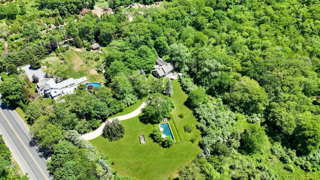 Vista aérea de una propiedad arbolada con un amplio césped y una piscina.