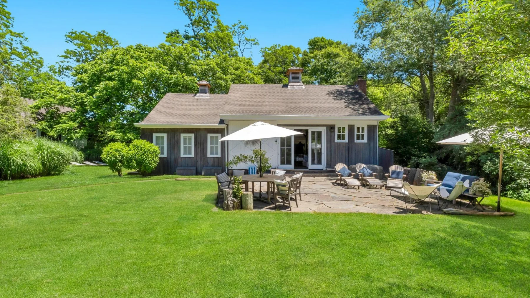 A house opens onto a patio with outdoor seating and a green lawn.