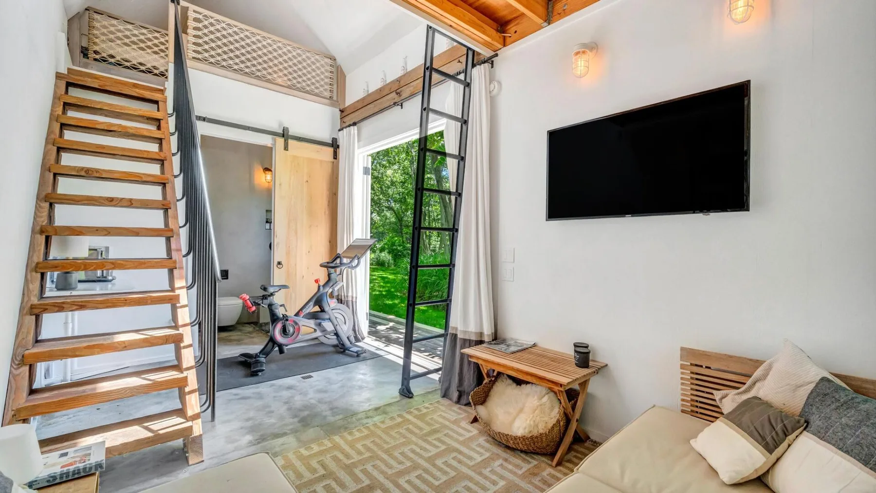 A bright loft bedroom with a wall-mounted television and exercise equipment.