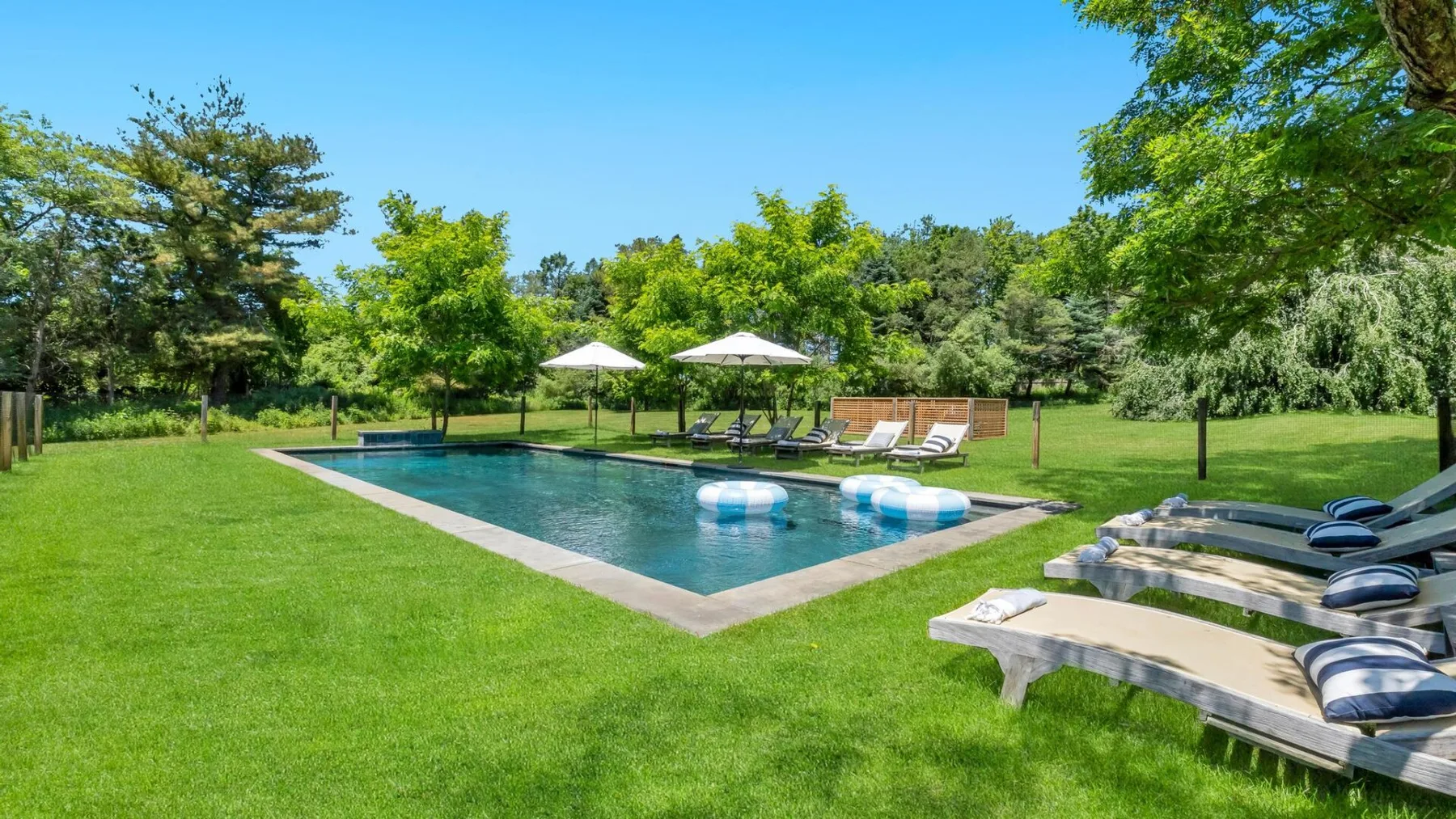 An outdoor swimming pool sits in a grassy lawn, with lounge seating nearby.