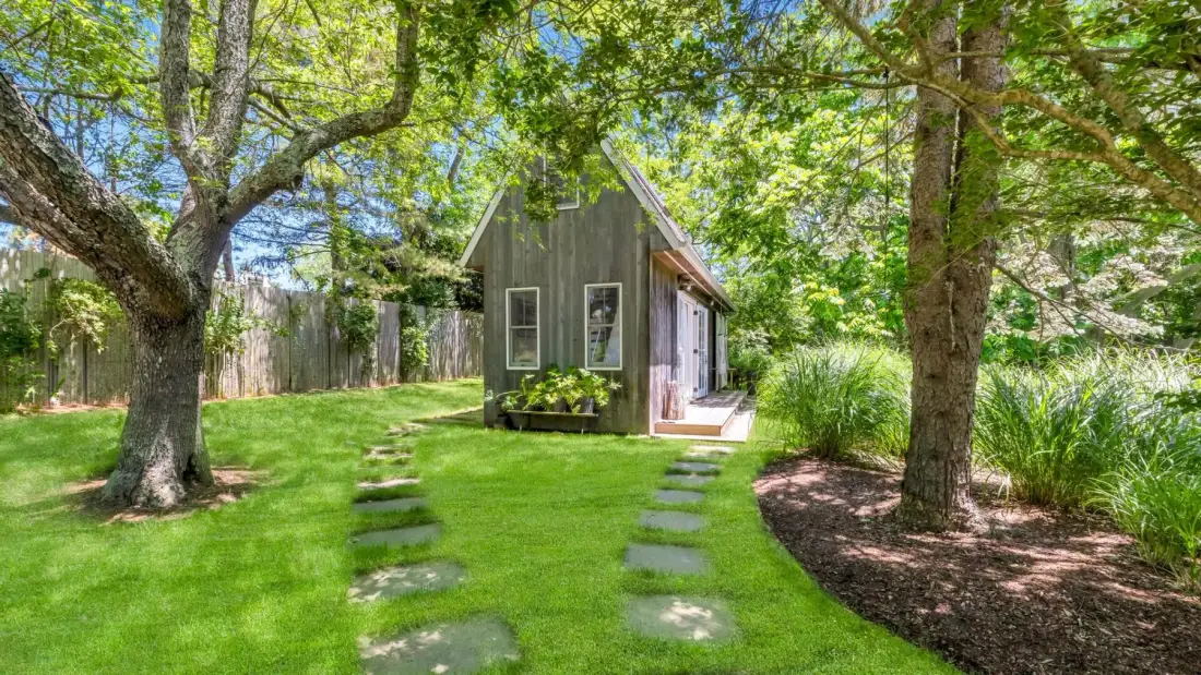 A small garden shed stands in a leafy lawn beside a stepping-stone path.