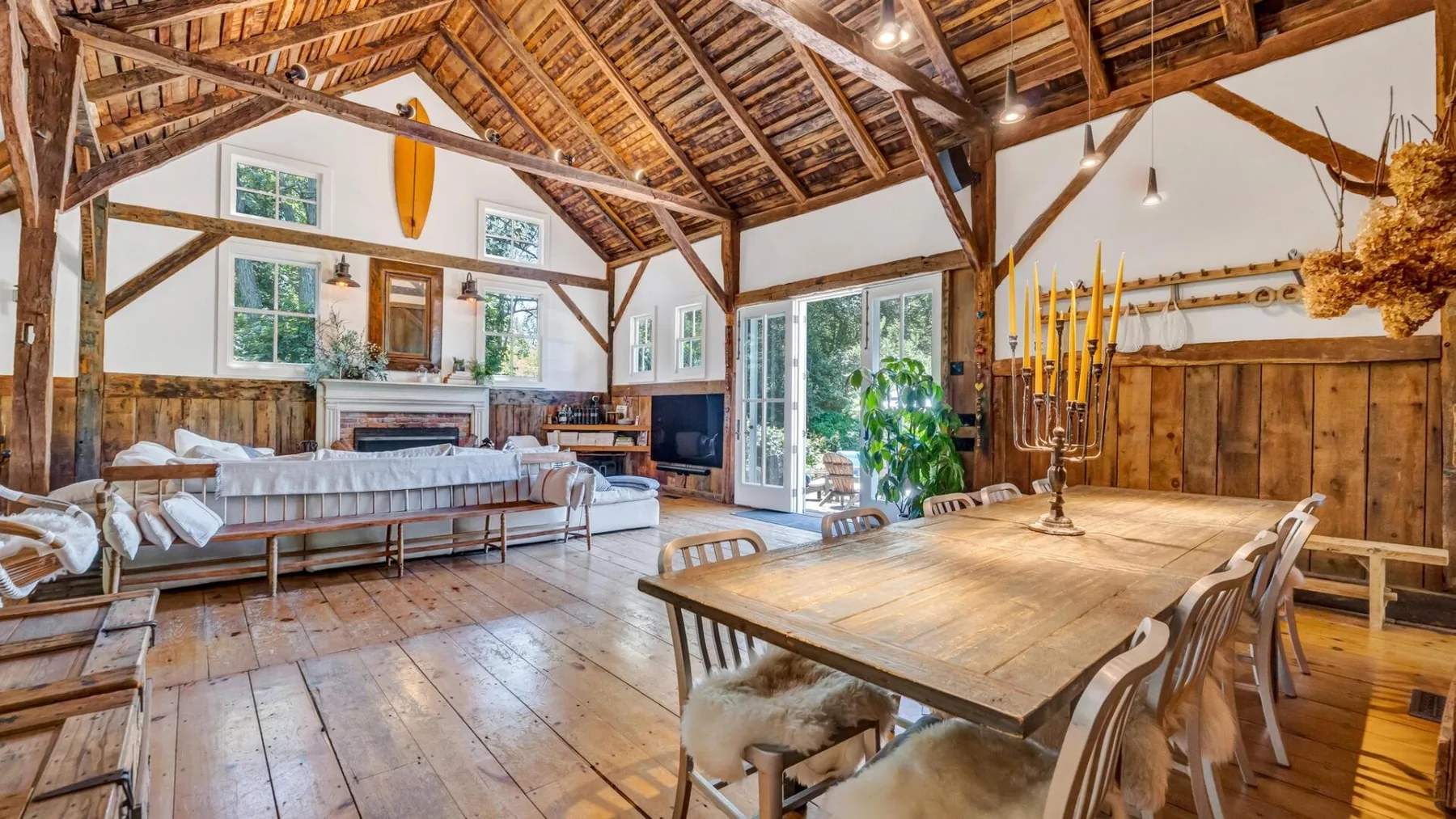 A rustic dining and living room with a long wooden table beneath exposed beams.