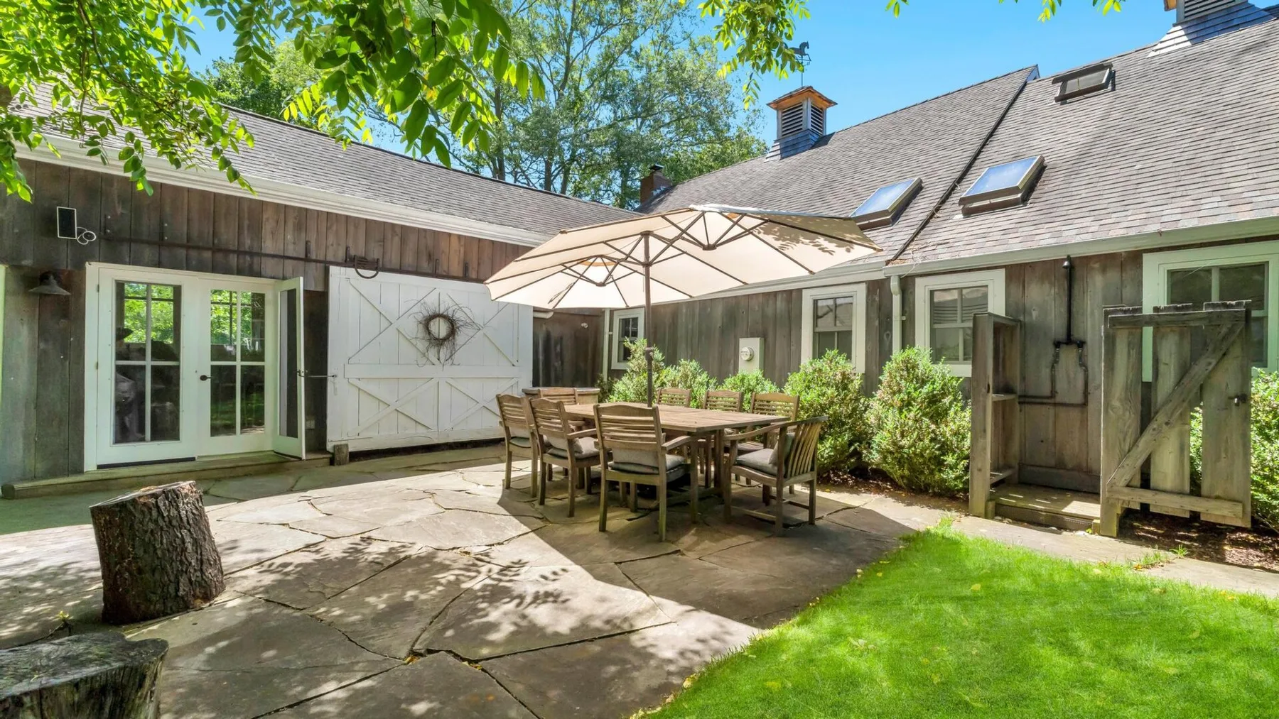 An outdoor patio with a dining table and umbrella beside a green lawn.