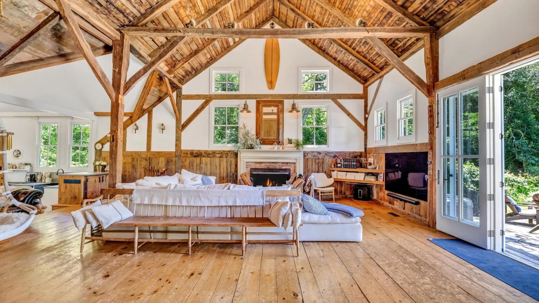 A spacious living room with exposed wooden beams, seating, and a fireplace.