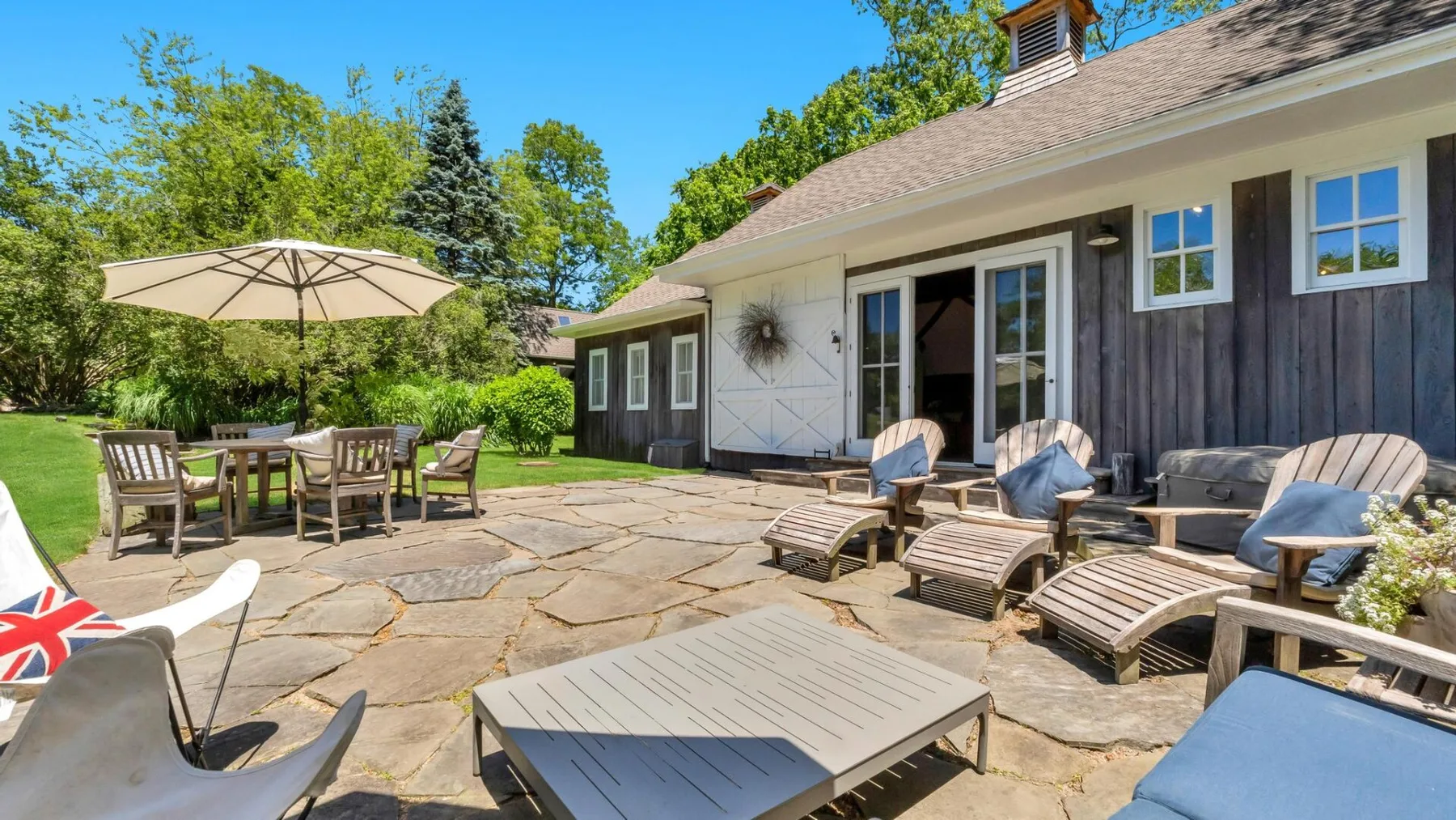 A sunny outdoor patio with lounge seating beside a house.