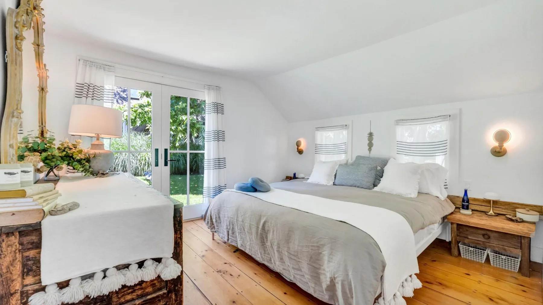 A bright bedroom with beds beside a large glass door opening onto greenery.