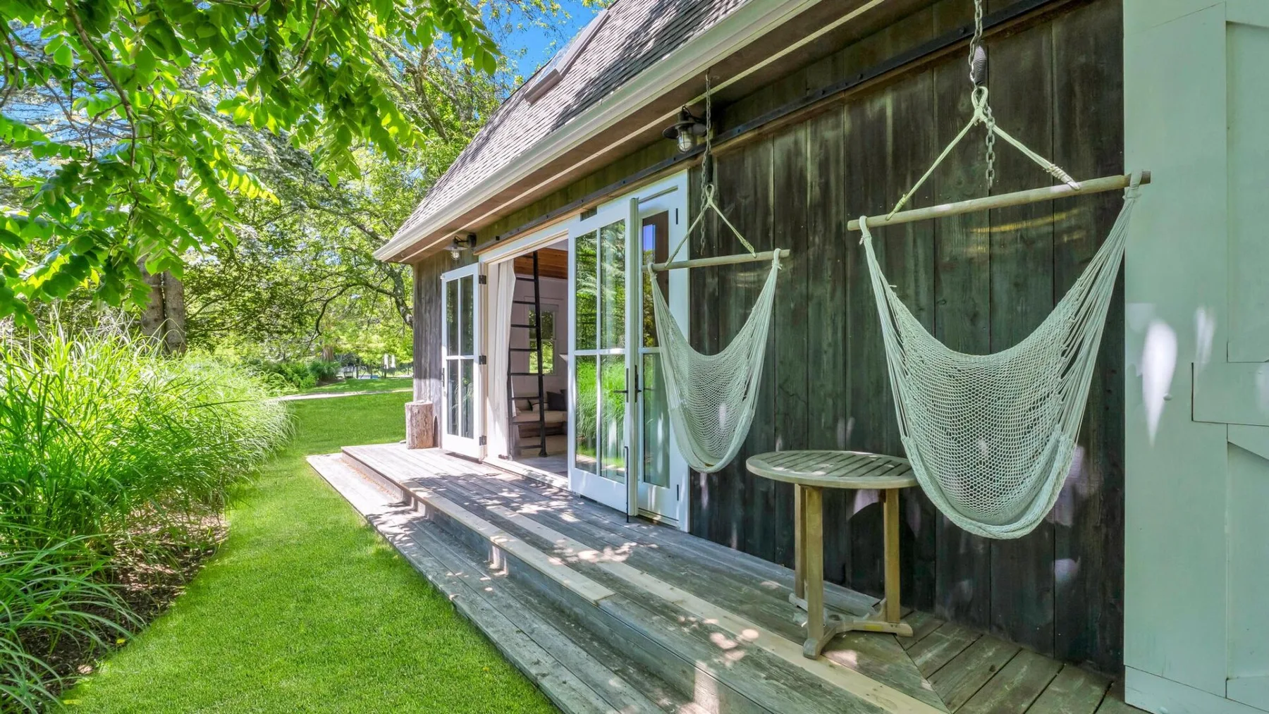 A garden-side deck with hanging hammocks beside an open glass door.