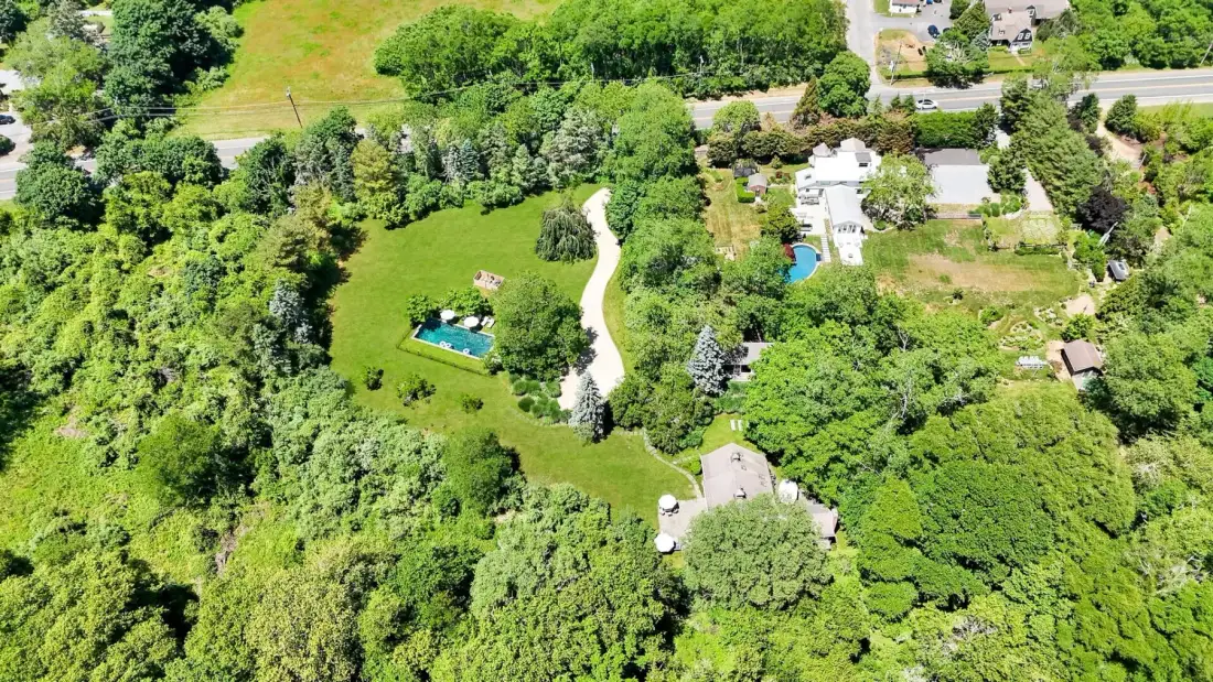 An aerial view of a wooded property with open lawns and a winding driveway.