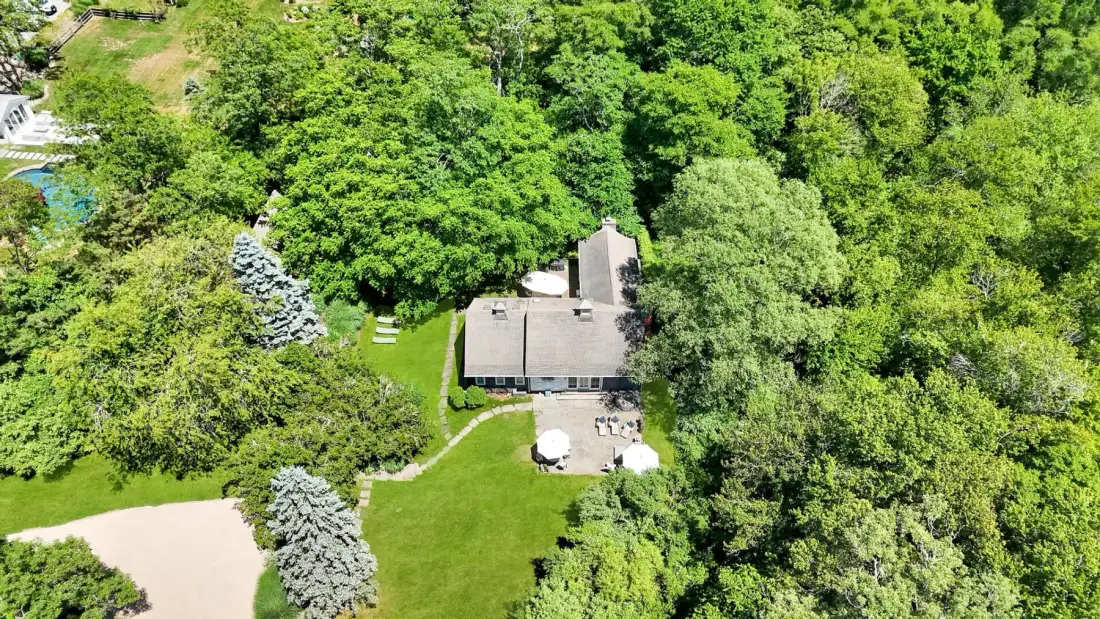 Aerial view of a house surrounded by dense trees and green lawn.