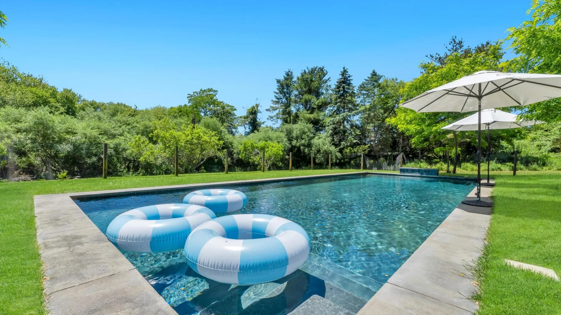 An outdoor swimming pool with inflatable rings and umbrellas beside the water.