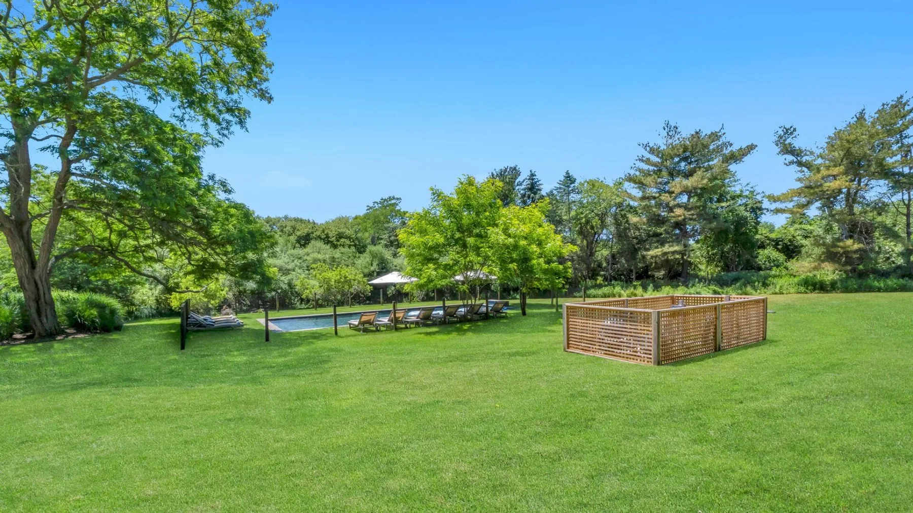 A grassy outdoor lawn with trees and a low wooden garden structure.