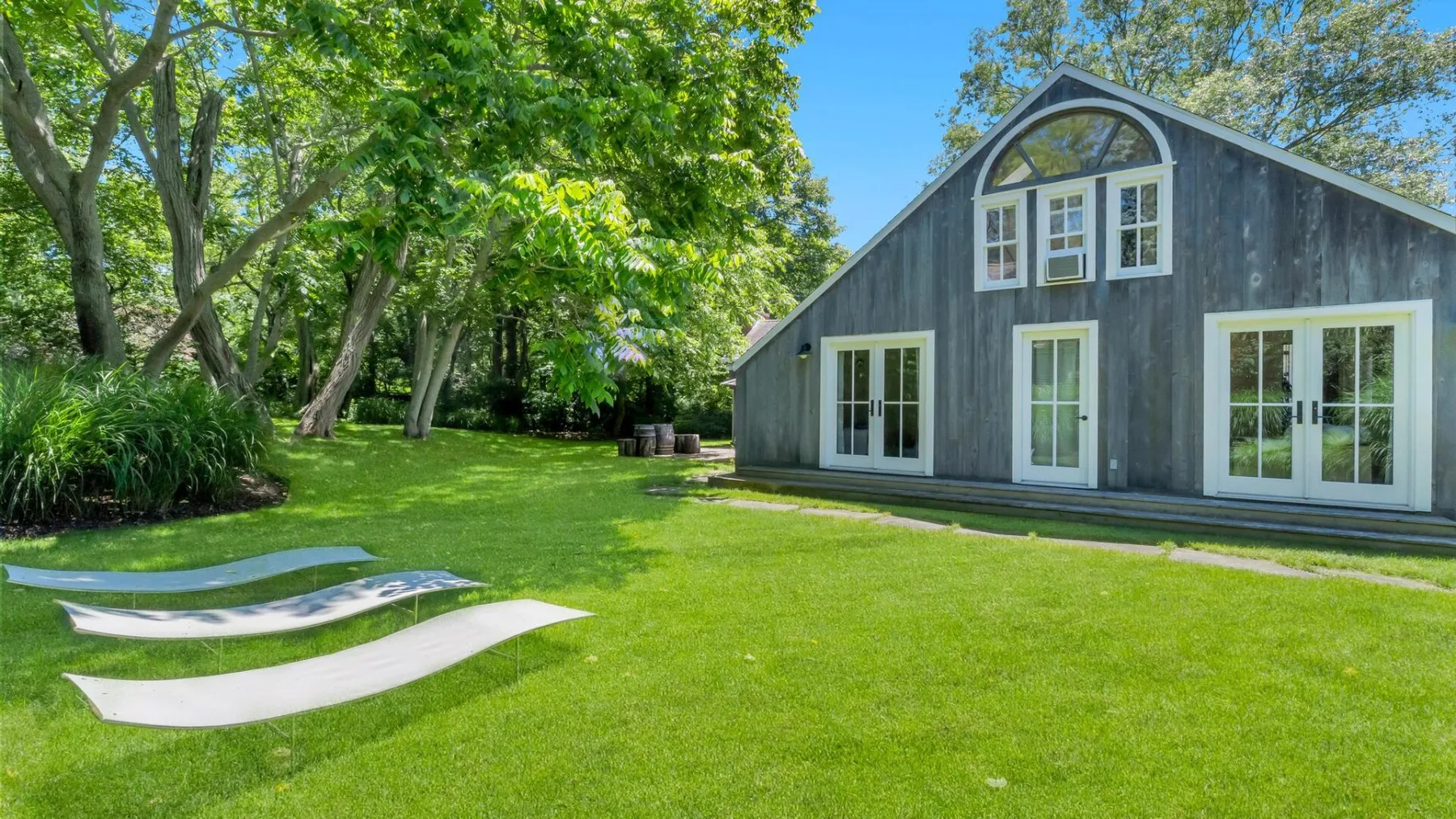 A dark gray barn-style building stands beside a broad green lawn and leafy trees.