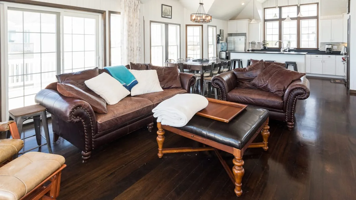 A living room with leather seating and a kitchen in the background.