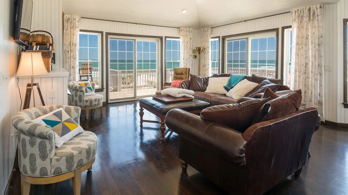 A bright living room with seating arranged around a coffee table beside large windows.