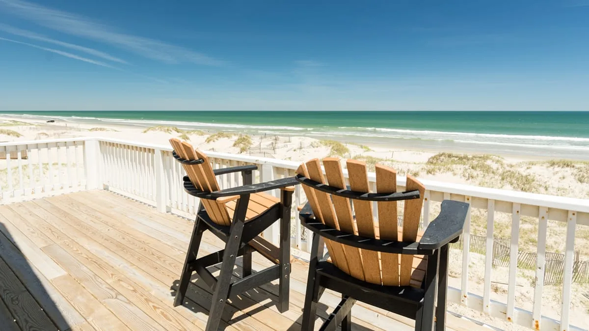 A beachside deck overlooks the ocean, with two wooden chairs beside the railing.