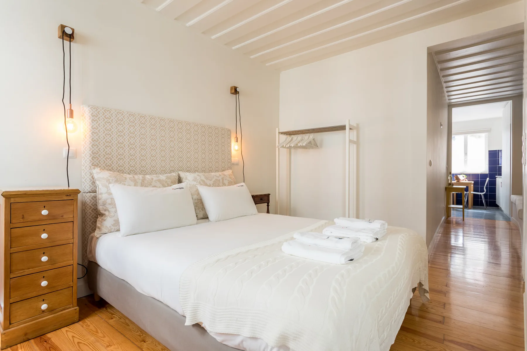 Un dormitorio luminoso con una cama bien hecha y suelo de madera.
