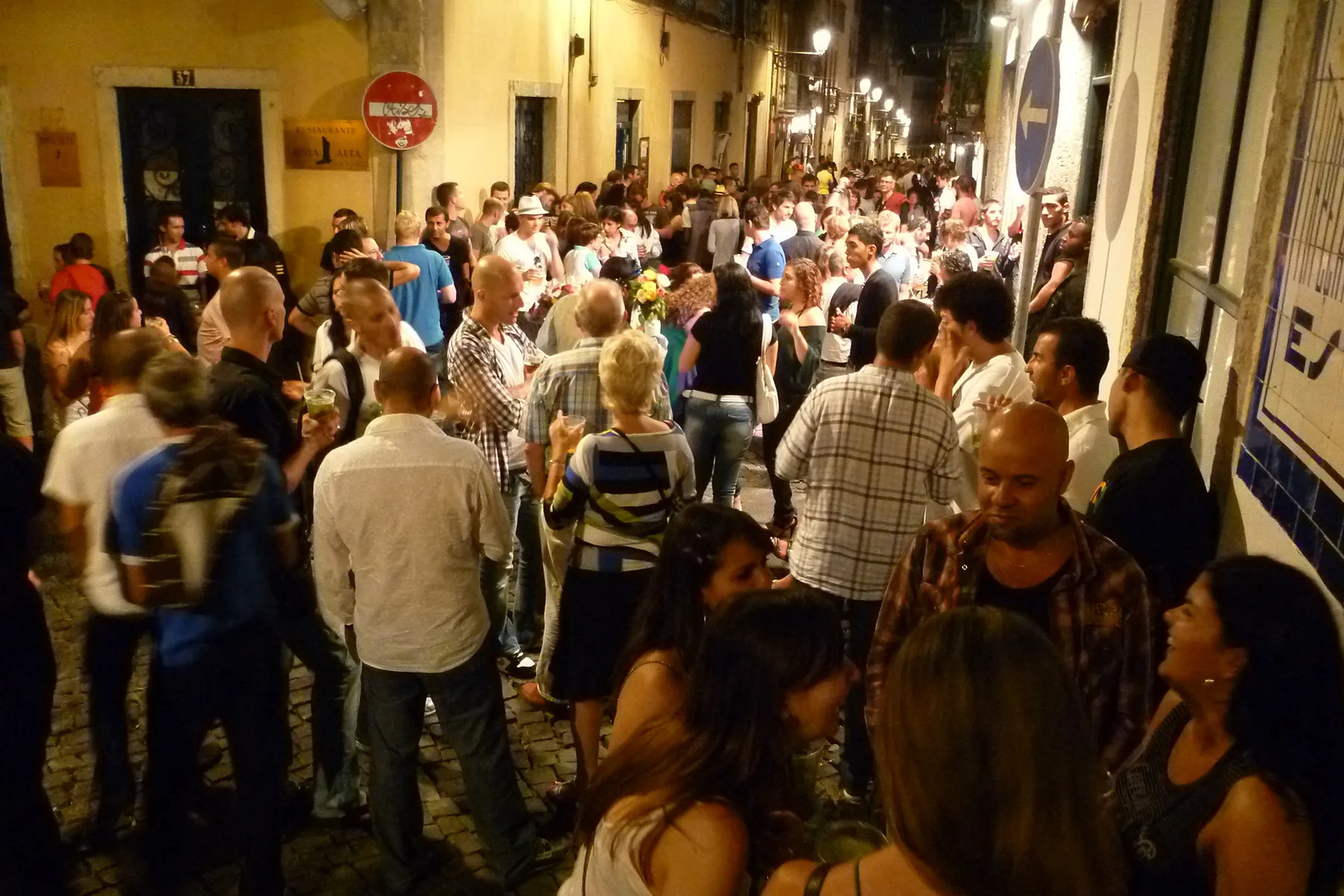 Una concurrida escena nocturna en una calle con gente reunida entre edificios cercanos.