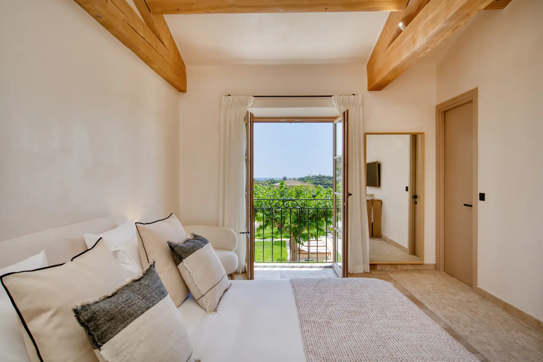 Un dormitorio luminoso con asientos junto a una puerta de balcón abierta con vistas a la vegetación.