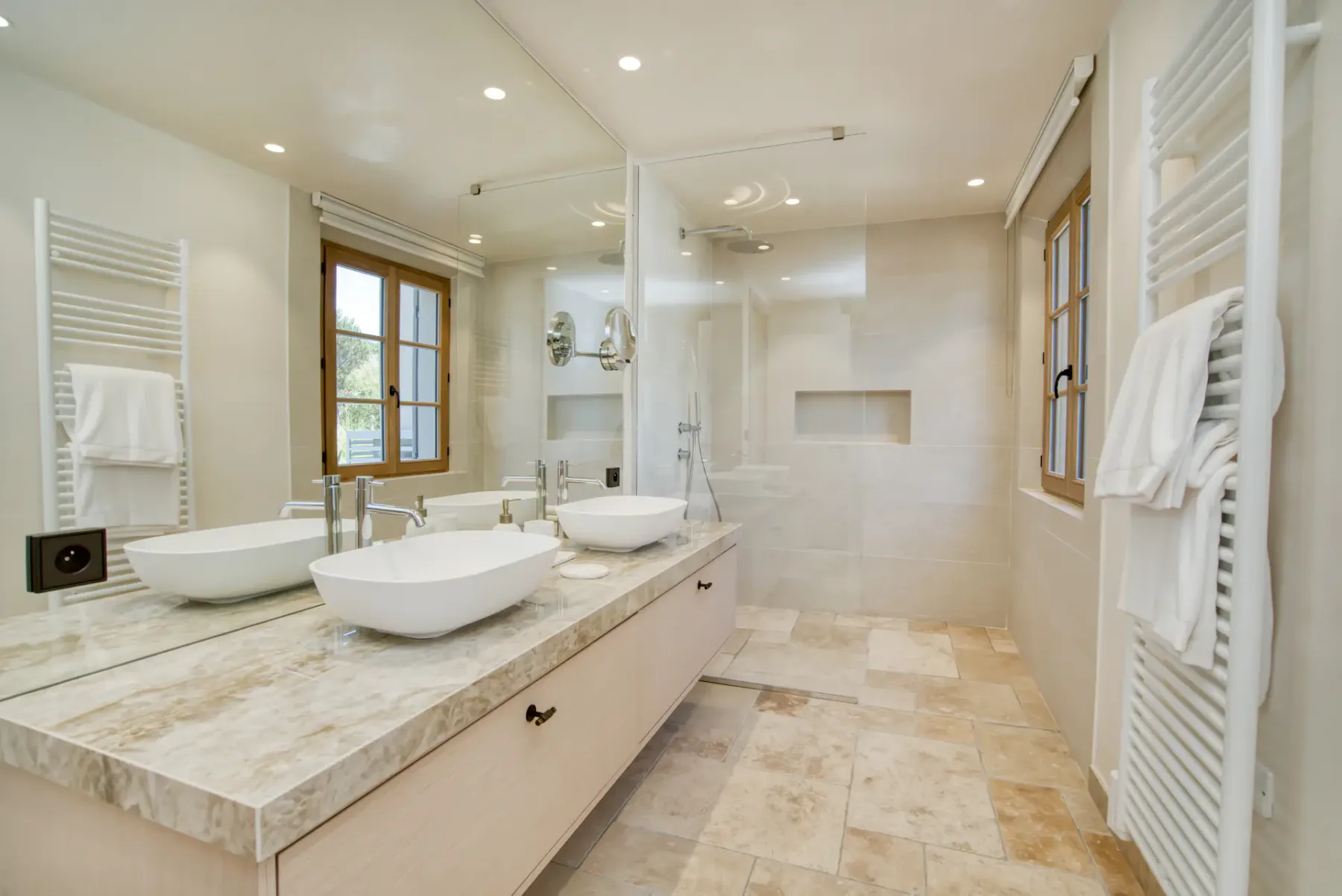 Un baño luminoso con un mueble largo, lavabos sobre encimera y una ducha de cristal.