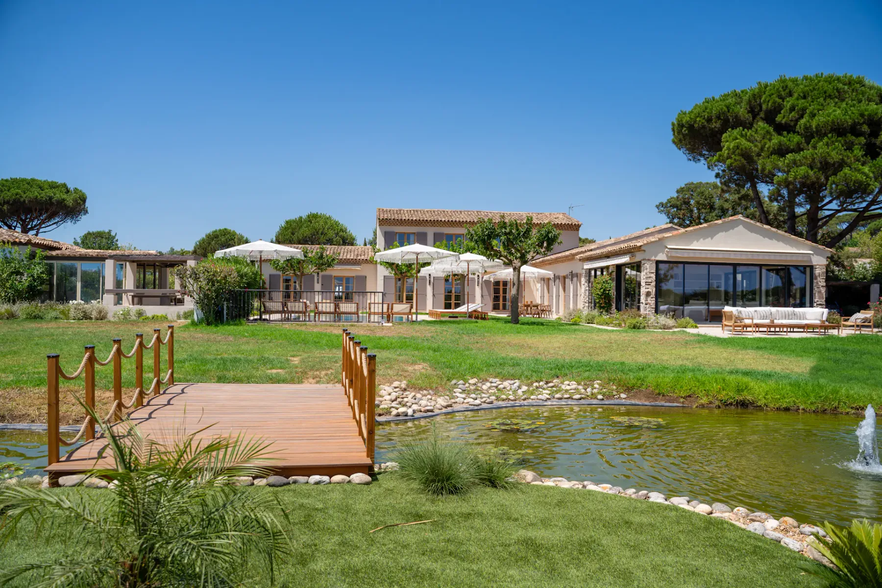 Un patio ajardinado de una villa con un puente de madera sobre un estanque.