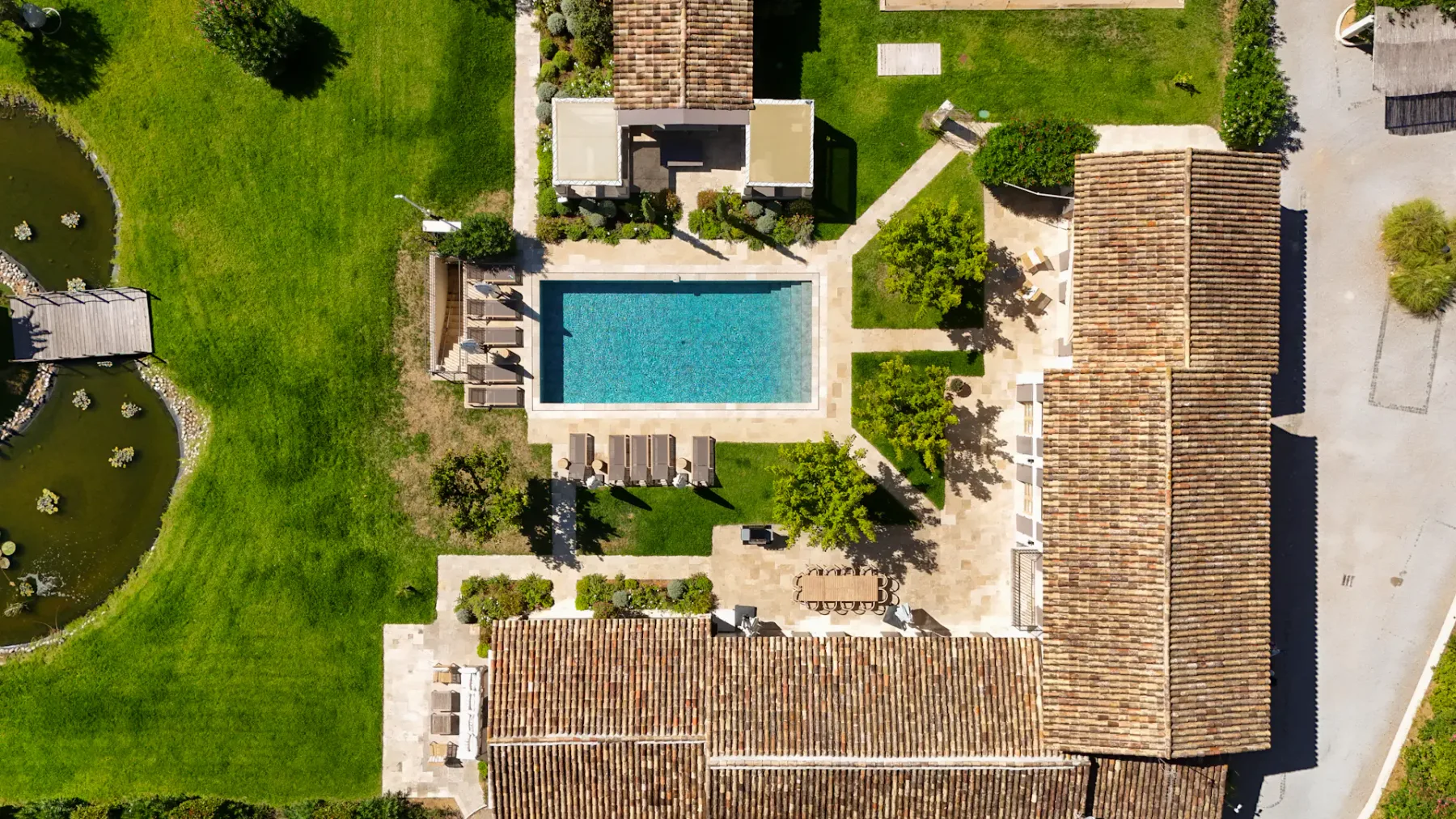 Vista aérea de una lujosa propiedad con una piscina azul en el centro, rodeada de vegetación y edificios con tejados de terracota.