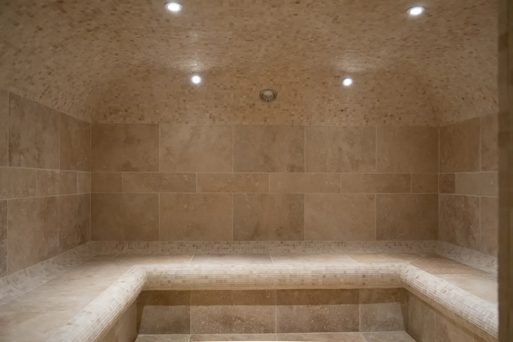 Un baño de vapor alicatado con asientos integrados y luces empotradas en el techo.