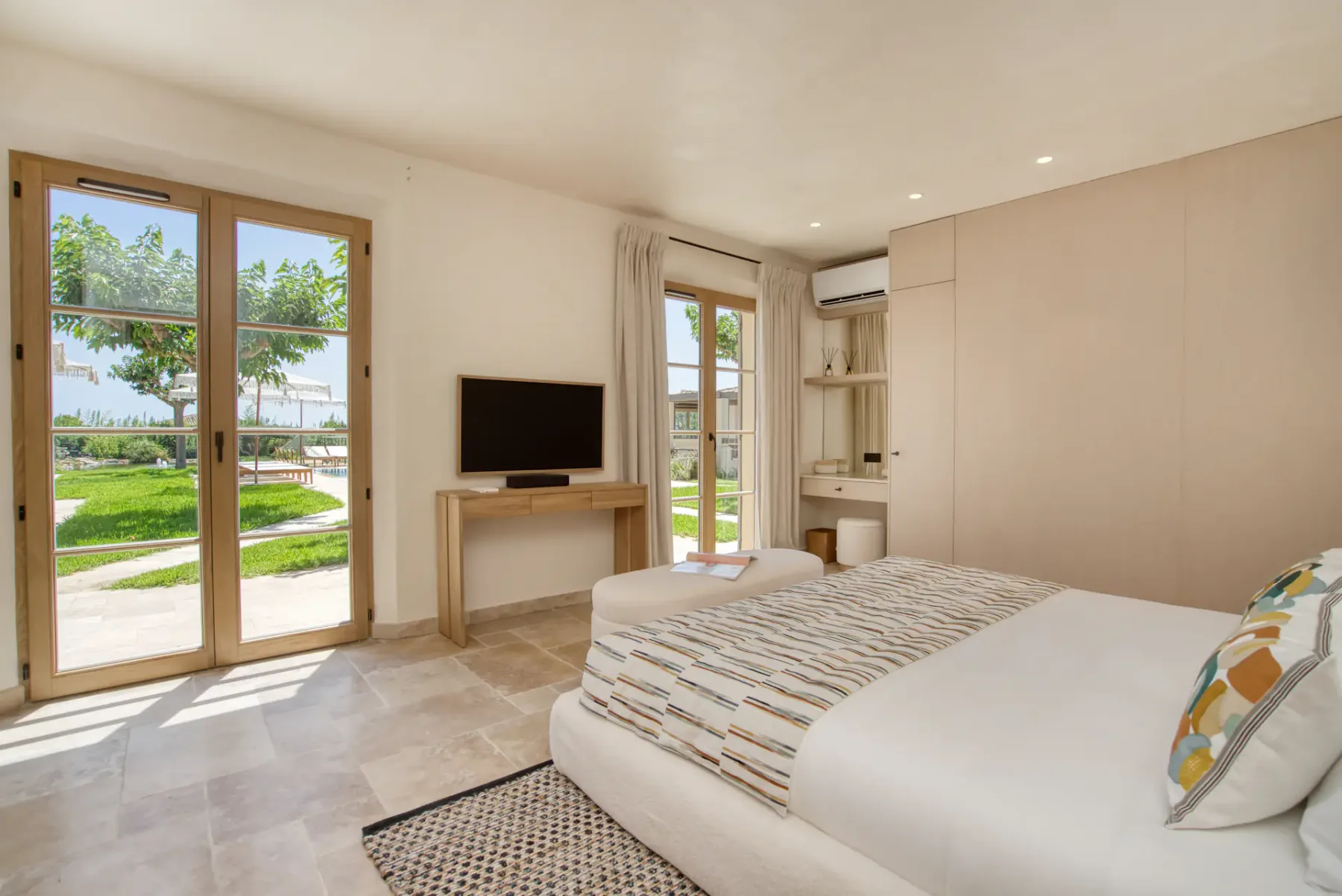 Un dormitorio luminoso con una cama grande, un televisor y puertas de cristal con vistas a la vegetación.