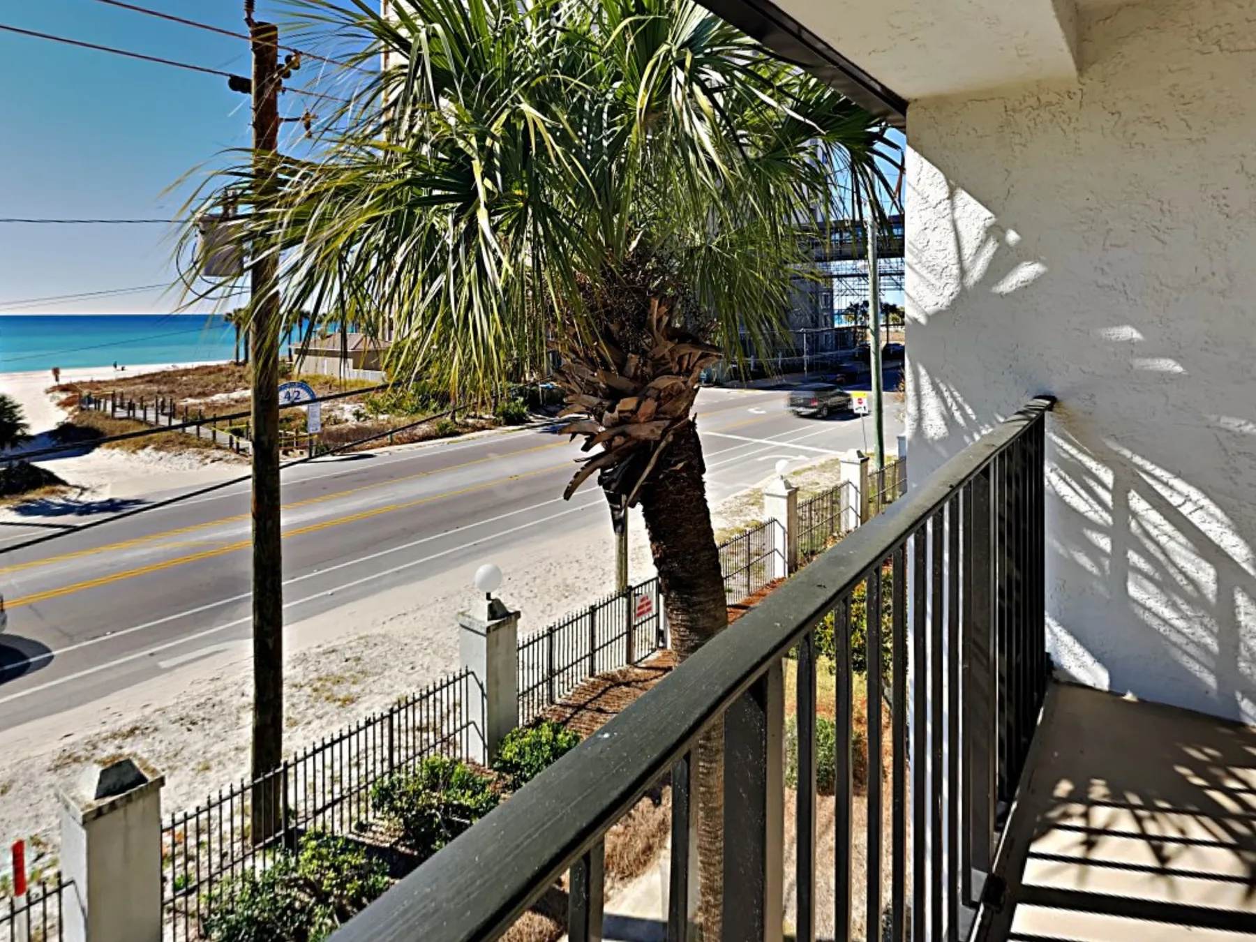A balcony overlooks a road, palm trees, and the ocean.