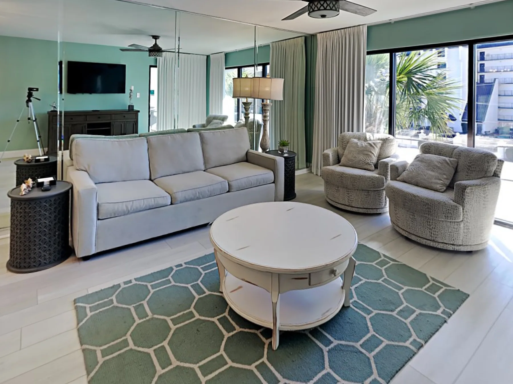 A bright living room with a sofa, two armchairs, and large windows.