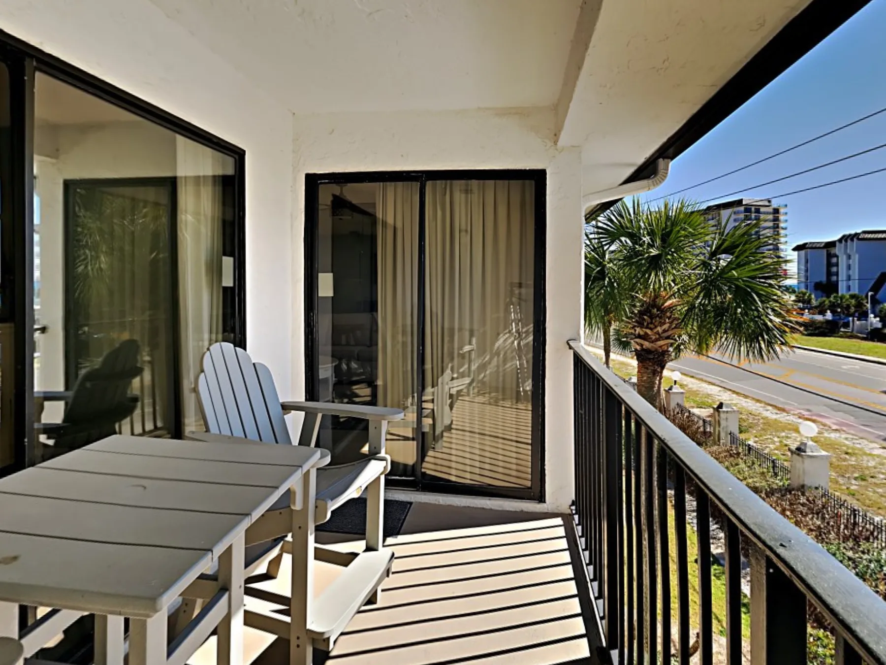 A balcony seating area overlooks a palm tree and the street.