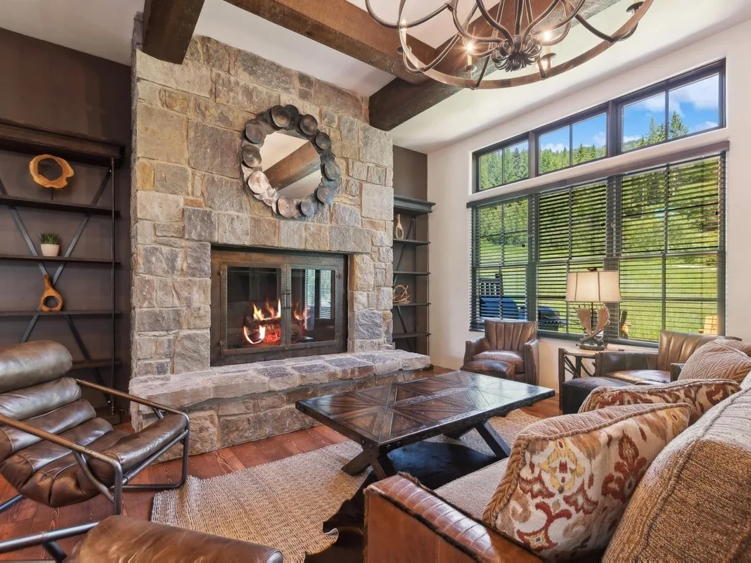Una sala de estar con chimenea de piedra, asientos y grandes ventanas.