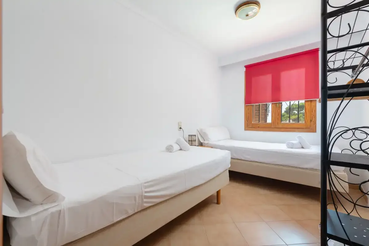 Un dormitorio con dos camas y una cortina roja en la ventana.